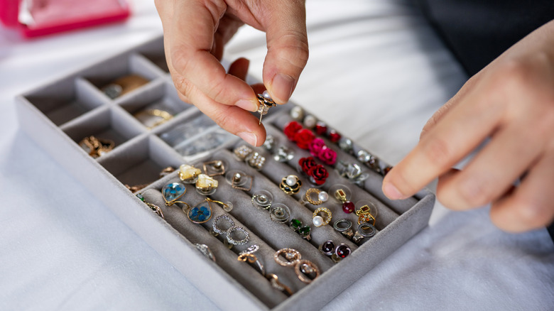 A woman takes out an earring from a cluttered jewelry box