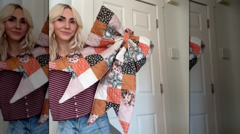 A woman holds up a large quilted bow made from quilt fabric.