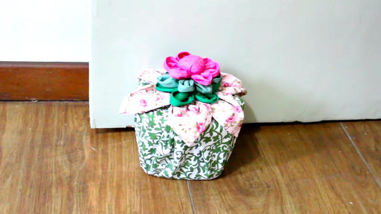 A fabric-wrapped doorstop made from a plastic container