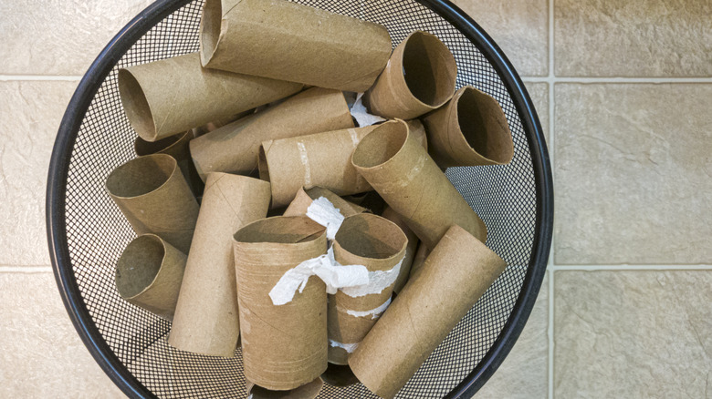 A black trash basket with empty toilet paper rolls in it.