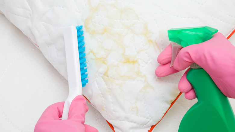 Hands holding green spray bottle near stained pillow
