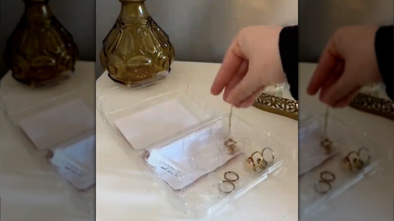 Woman's hand lacing long necklace chain into clear plastic cupcake container.
