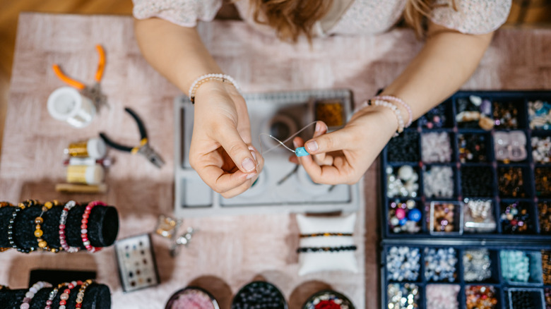 Young woman making jewelry with beads in her home.