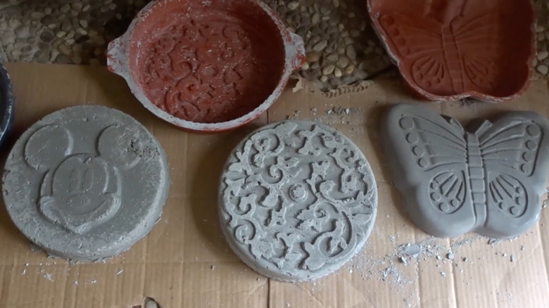Three concrete pavers sit on the ground near decorative old cake tins
