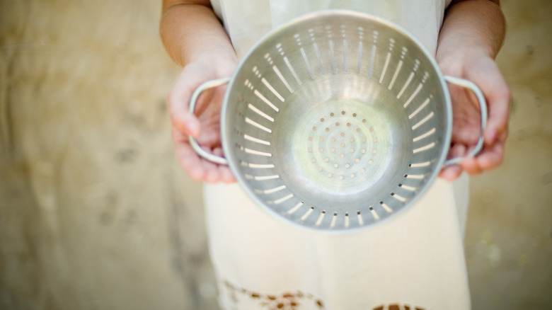 A person holds an old colander