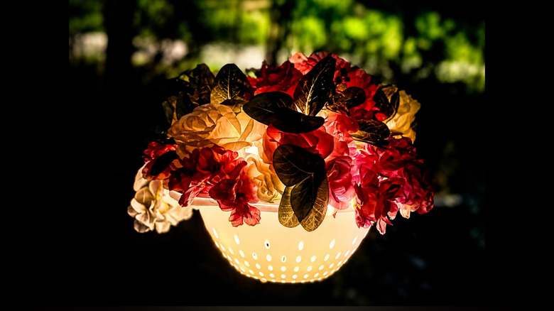 A DIY colander lamp covered in faux flowers glows at night