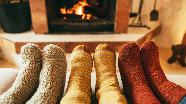 Three pairs of feet wearing cozy socks in front of a fireplace
