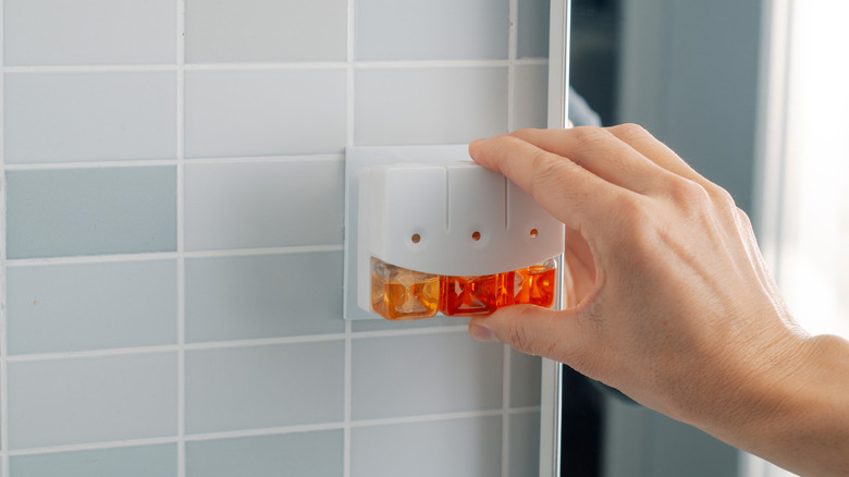 Hand plugging an air freshener into a wall outlet