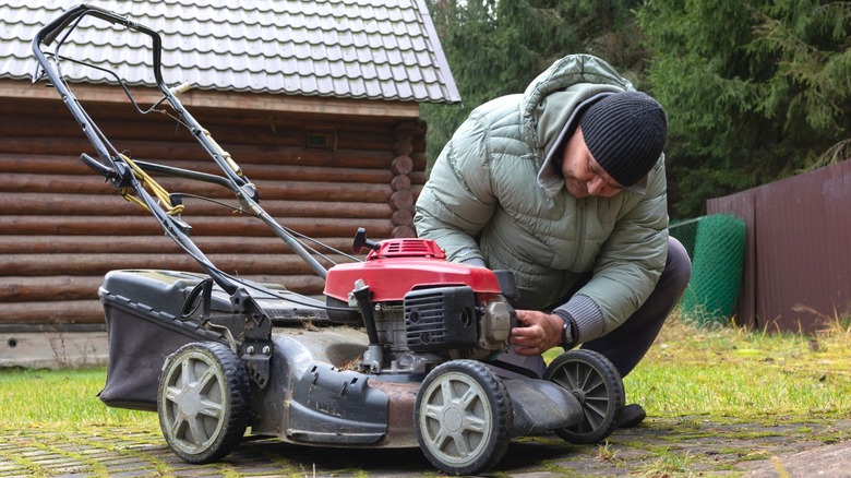 Man in heavy jacket performing maintenance on lawn mower in the fall