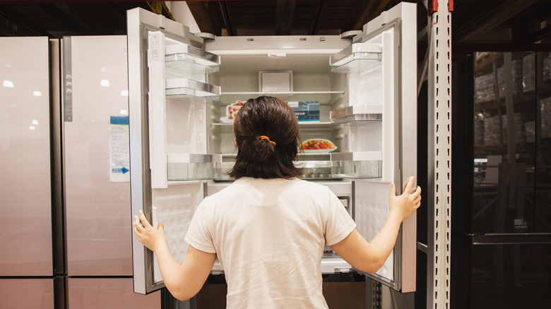 woman shopping for a refrigerator in a store with doors opened and back facing us