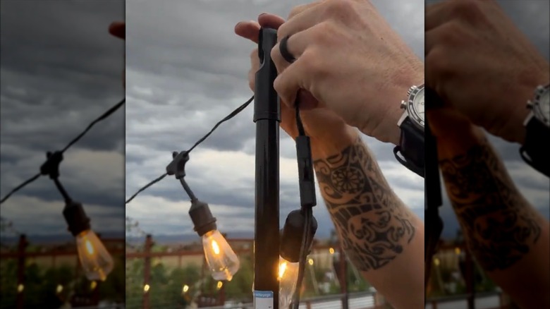 Person attaching string lights to the end of a broom handle