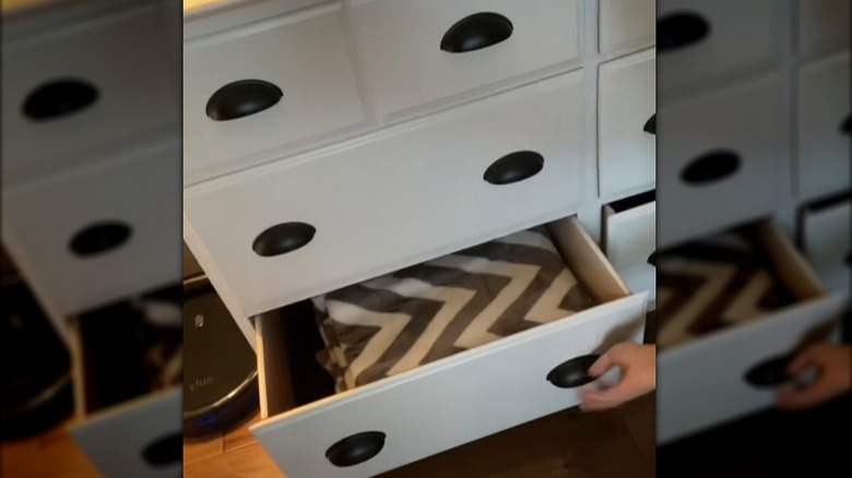 Person showing blankets being stored in a dresser behind the couch in the living room