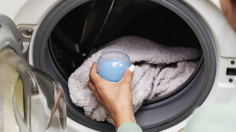 Person adding liquid detergent to the drum of a washing maching