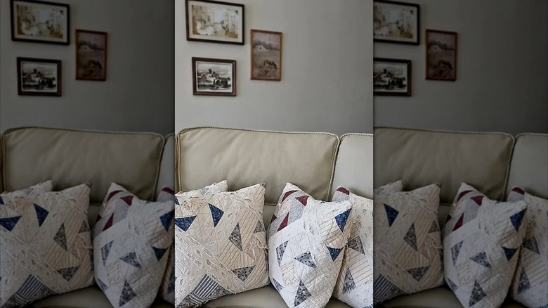 Vintage quilted throw pillows on a tan couch in front of white walls with pictures.