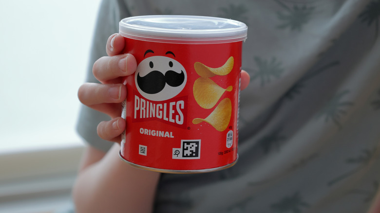 An unidentifiable person in a grey shirt holding a small can of pringles