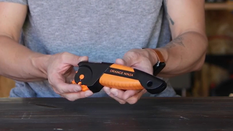 A person holding the Orange Ninja multi-tool sharpener over a black work bench