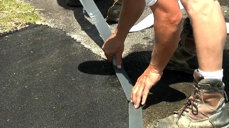 A person applying asphalt repair tape to a crack