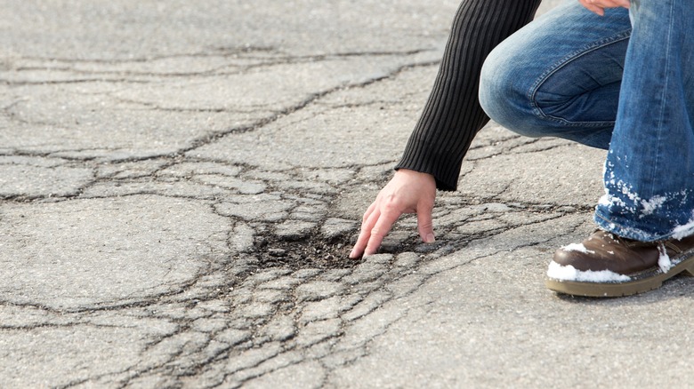 Person inspecting asphalt driveway pothole needing repair