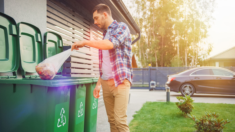 Person throwing trash in a can outside their house