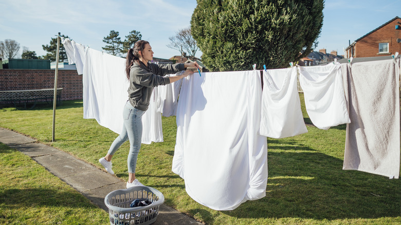 Person hanging white sheets on the clothesline in yard