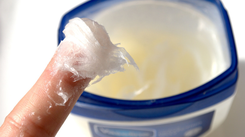 A finger covered in petroleum jelly from a Vaseline container