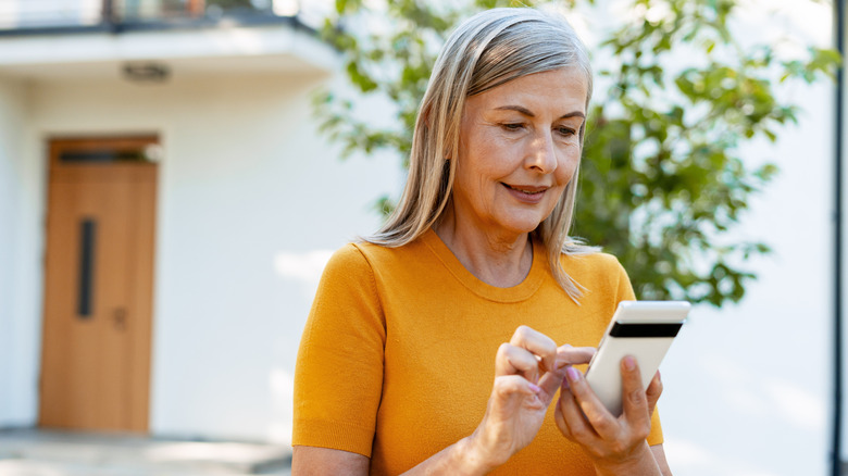 A woman makes a purchase on her phone outside her home