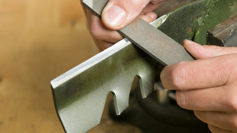 Hands sharpening a blade with a metal file.