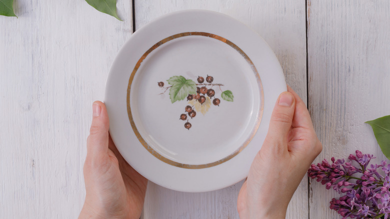 A woman holds a floral plate against a wooden table