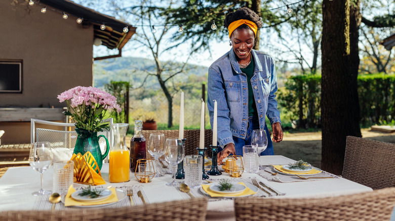 A smiling woman sets an elegant patio table on a sunny day