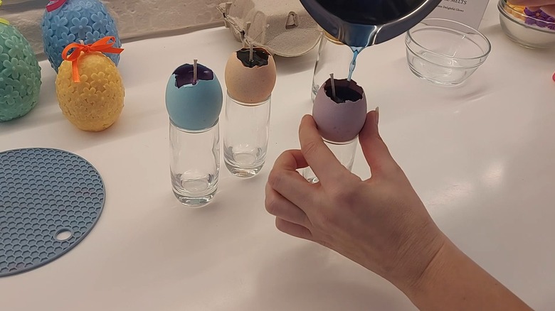 Hand pouring in colored melted wax inside a colored eggshell with wick attached