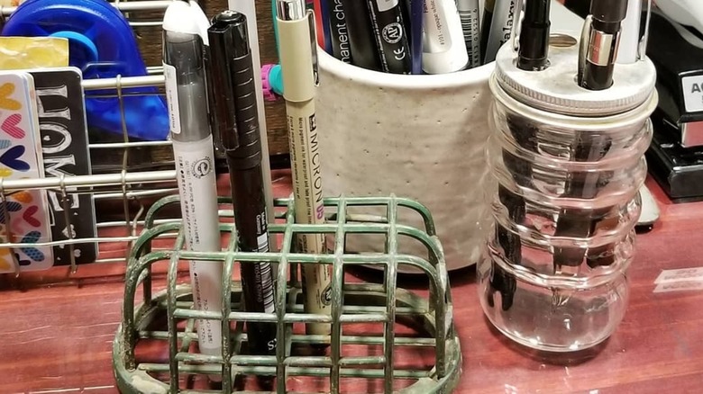 Collection of desk organizers, including a vintage spice jar with pens in it
