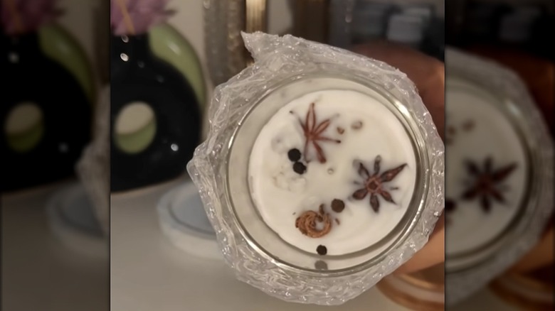 Close-up of a candle made in a wide-mouth spice jar with dried spices in the wax