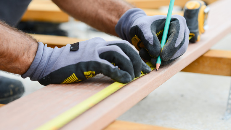 a person marks a measurement on a wood plank