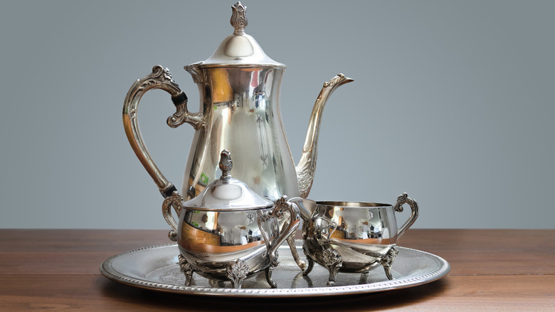 An ornate silver tea set sits on a wooden table