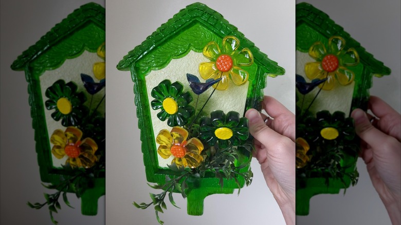 A vintage lucite wall plaque featuring a green birdhouse, green and yellow flowers, and a blue bird