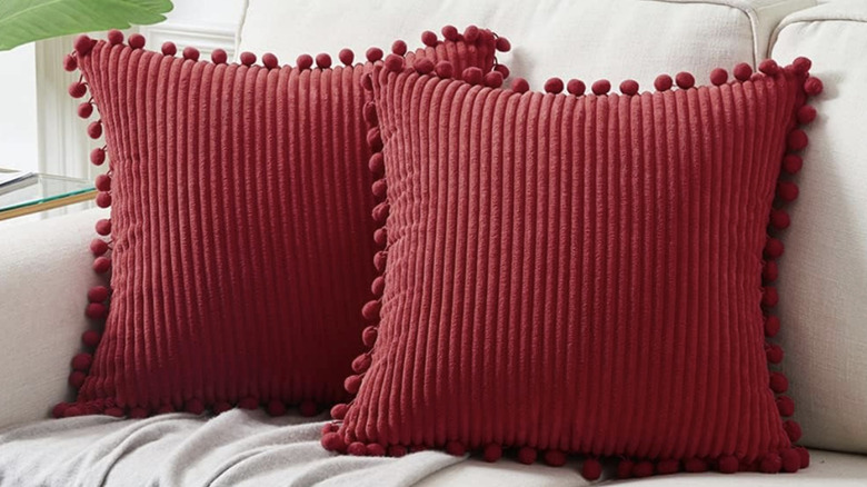 Two red throw pillows with tassels on a white sofa