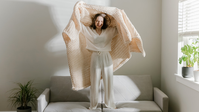 Young woman standing on couch with blanket.