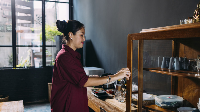 A woman smiles while opening a wood cabinet