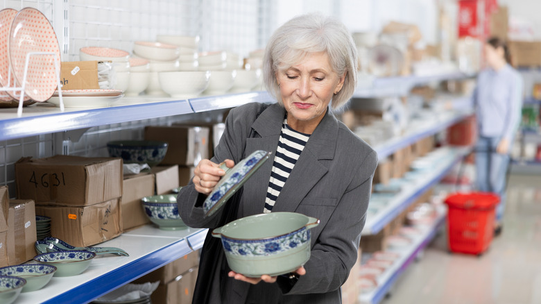 An elderly woman looks at a lidded pot at a thrift store