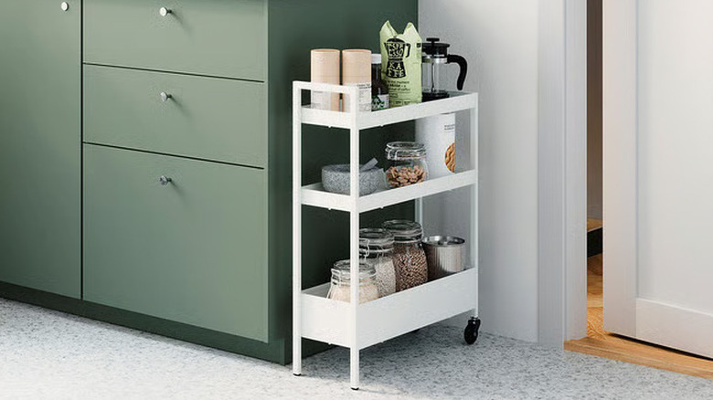 A small white rolling storage cart sits next to a sage green cabinet
