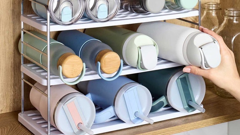 A woman's hand reaches for a YouCopia water bottle organizer inside a cabinet