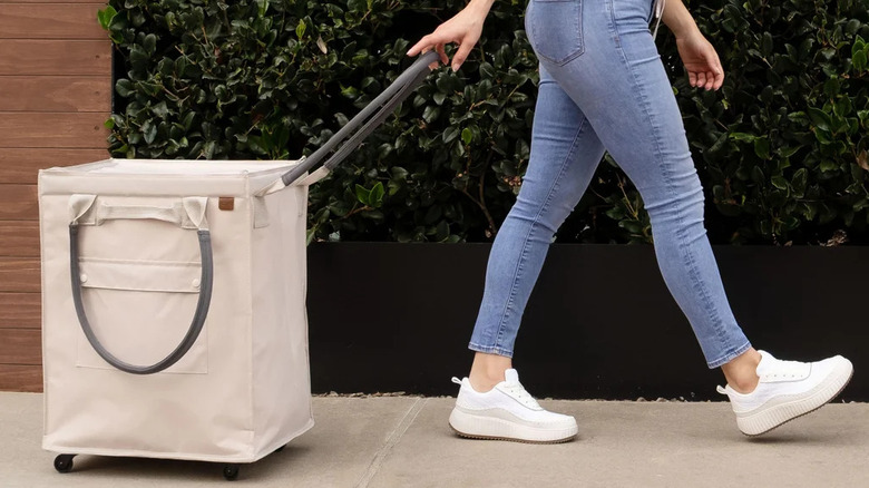 A person pulls a cream-colored foldable tote bag on wheels
