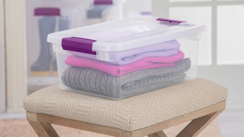 Folded sweaters are stored in a plastic box with purple latched handles