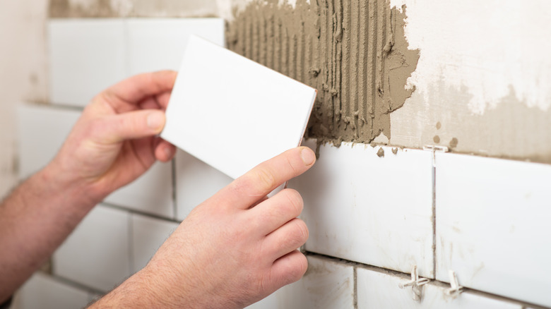 a worker lays a white tile on a wall