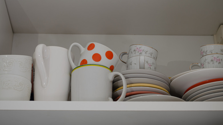 A cabinet with coffee mugs stacked on each other and plates