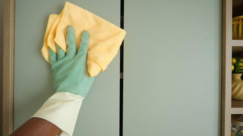 a gloved hand cleans a cabinet door