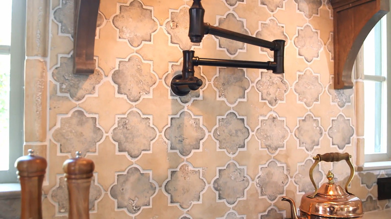 A stove backsplash with a bronze pot filler, a copper kettle, and a rustic tiles.