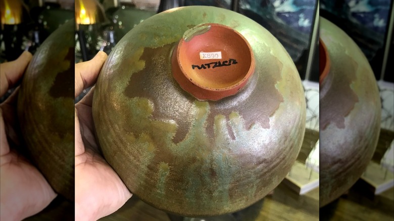 A person holds a green Natzler bowl upside-down to show the artist mark and archive number