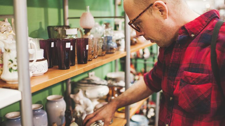 A man looks at thrift store shelves full of glassware and ceramics