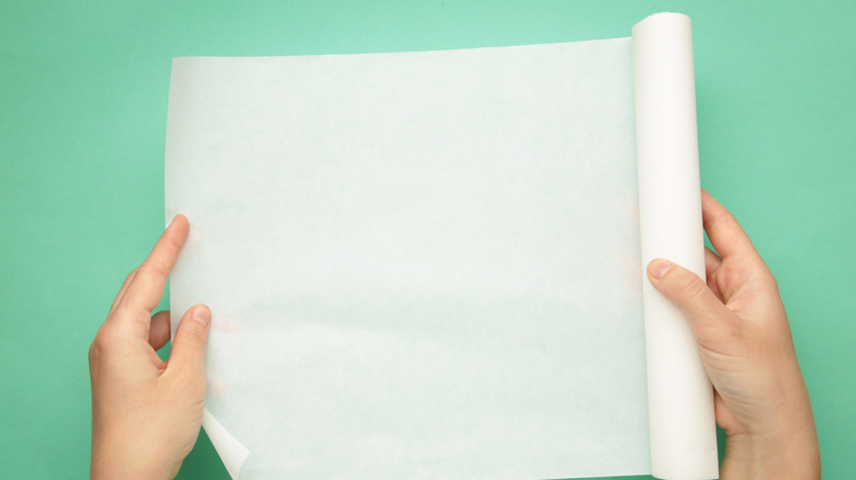 Person holding roll of wax paper with green background